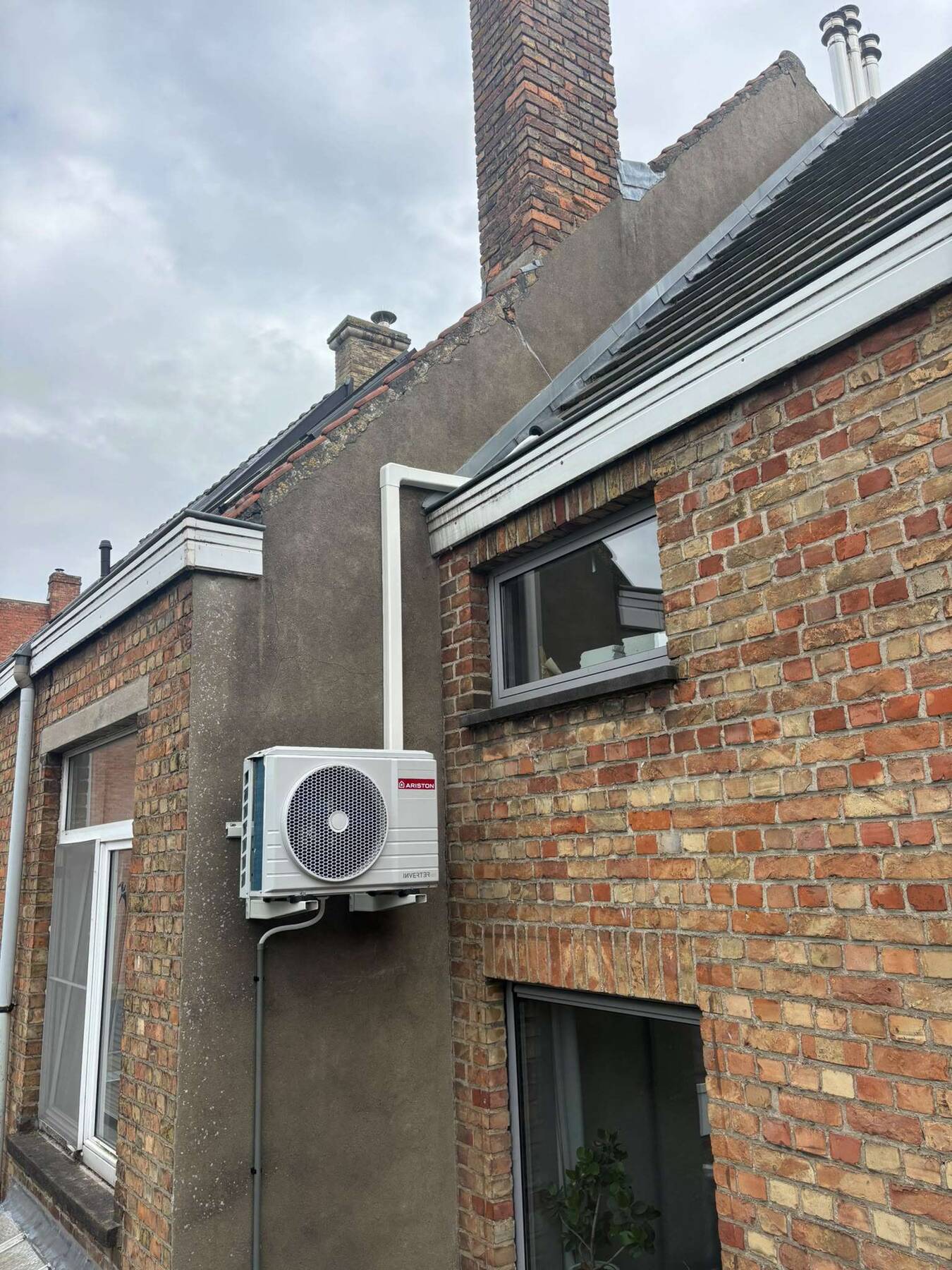 Ariston-buitenunit van een split-warmtepompboiler tegen de gevel in Brugge